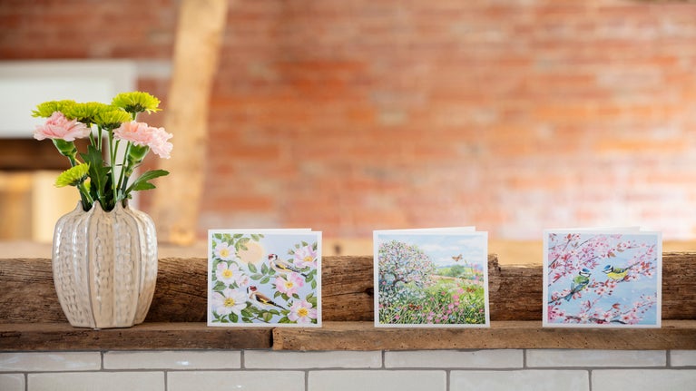An image showing a vase with flowers and three greeting cards